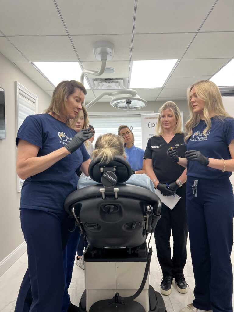 Students and instructor surrounding a live model who sits half inclined on a medical chair.